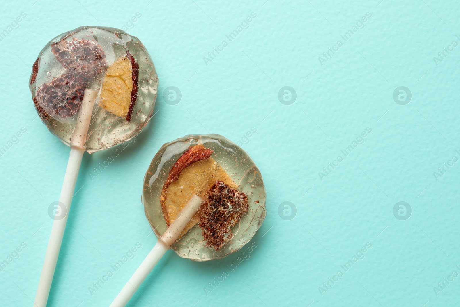 Photo of Sweet colorful lollipops with berries on turquoise background, flat lay. Space for text