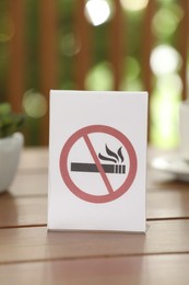 Photo of No Smoking sign on wooden table outdoors, closeup