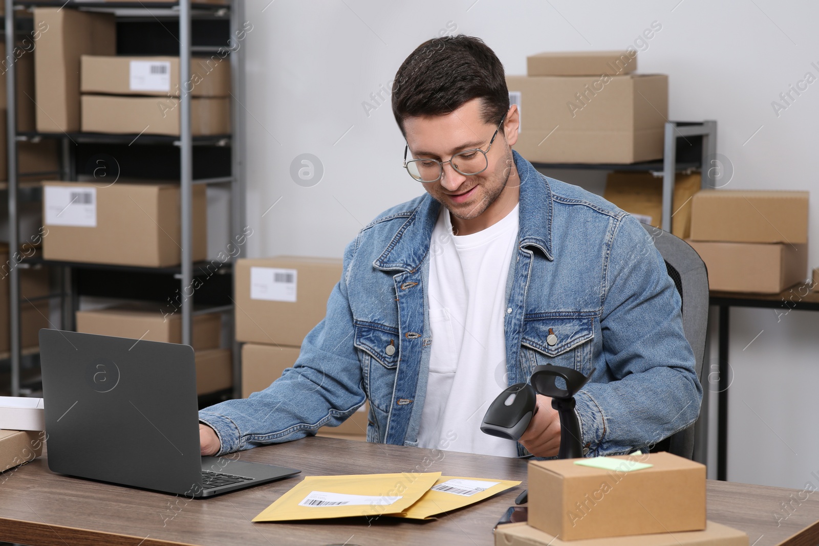 Photo of Seller with scanner, parcels and laptop at table in office. Online store