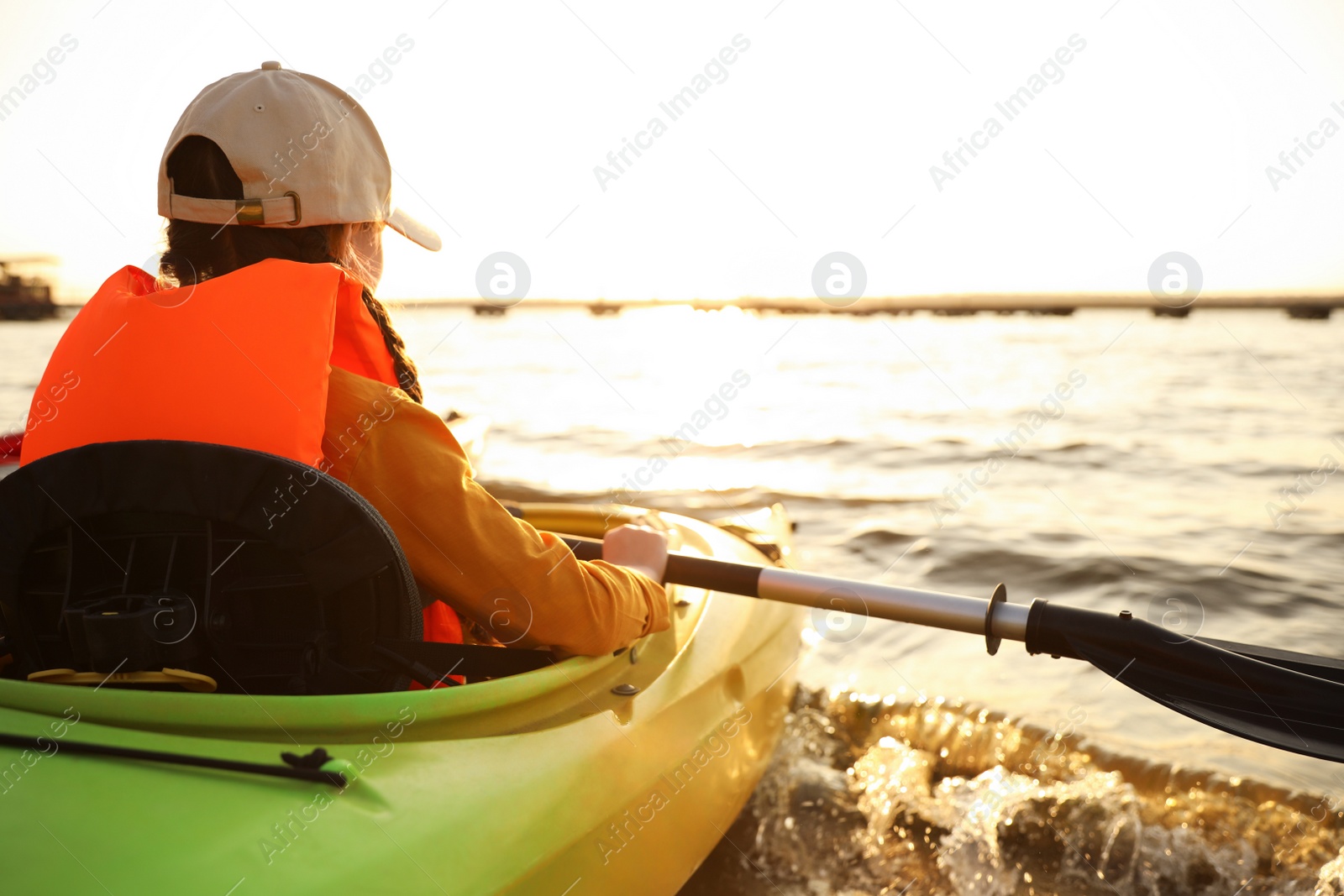 Photo of Little girl kayaking on river, back view. Summer camp activity