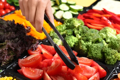 Photo of Young woman taking tomatoes from salad bar, closeup