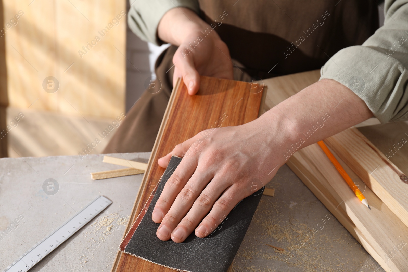 Photo of Man polishing wooden plank with sandpaper at grey table indoors, closeup