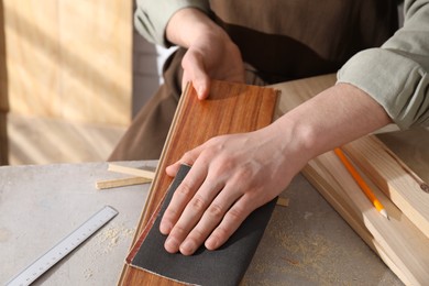 Man polishing wooden plank with sandpaper at grey table indoors, closeup