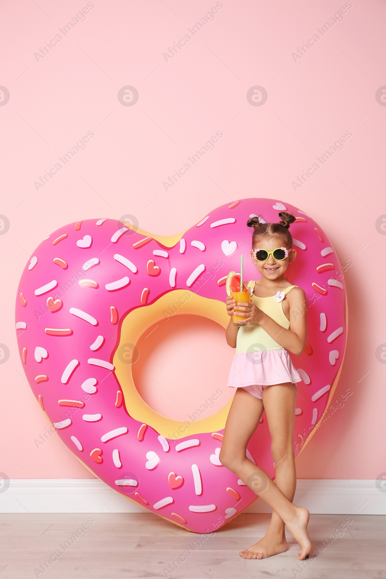 Photo of Cute little girl with inflatable heart and glass of cocktail near color wall