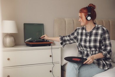 Photo of Young woman listening to music with turntable in bedroom