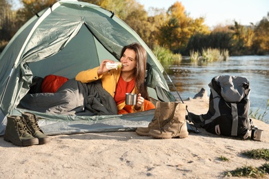 Young woman having breakfast in sleeping bag inside of camping tent