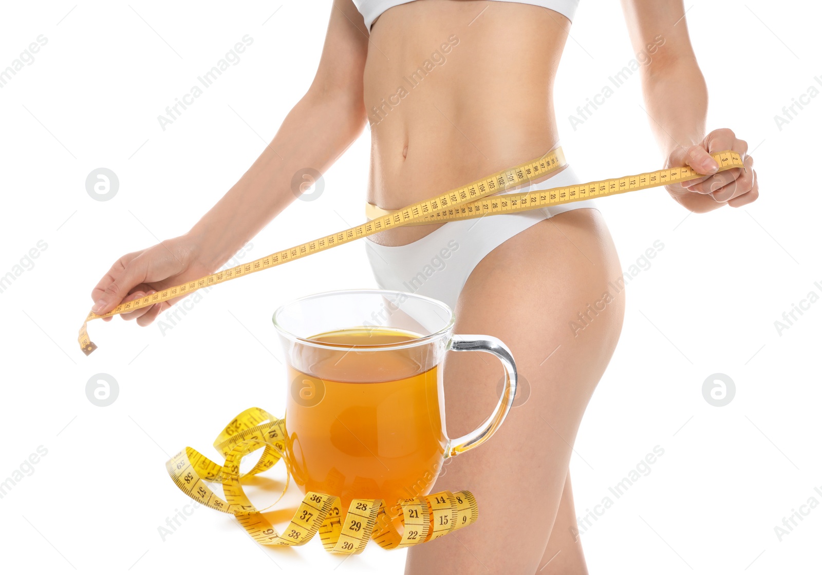 Image of Slim young woman with measuring tape and glass cup of weight loss herbal tea on white background