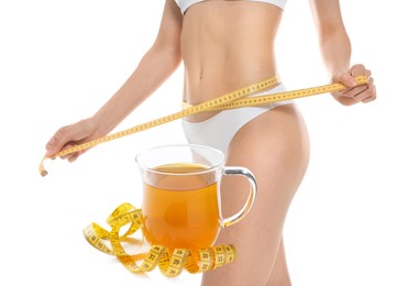 Image of Slim young woman with measuring tape and glass cup of weight loss herbal tea on white background