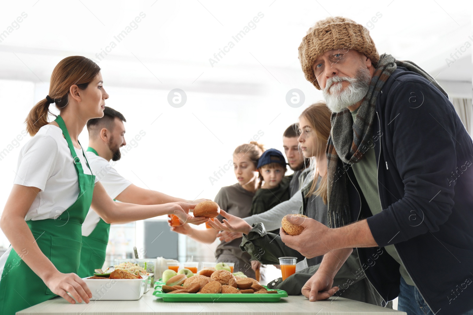 Photo of Senior man with other poor people receiving food from volunteers indoors
