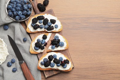 Photo of Tasty sandwiches with cream cheese, blueberries and blackberries on wooden table, flat lay. Space for text