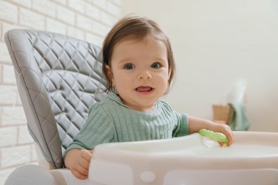 Cute little baby with teether in high chair indoors