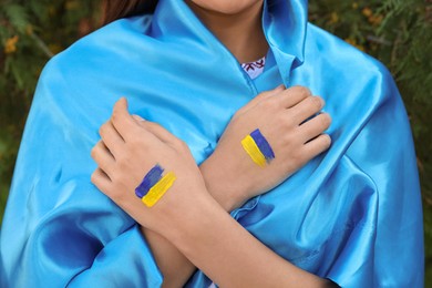 Photo of Woman with drawings of Ukrainian flag on hands outdoors, closeup