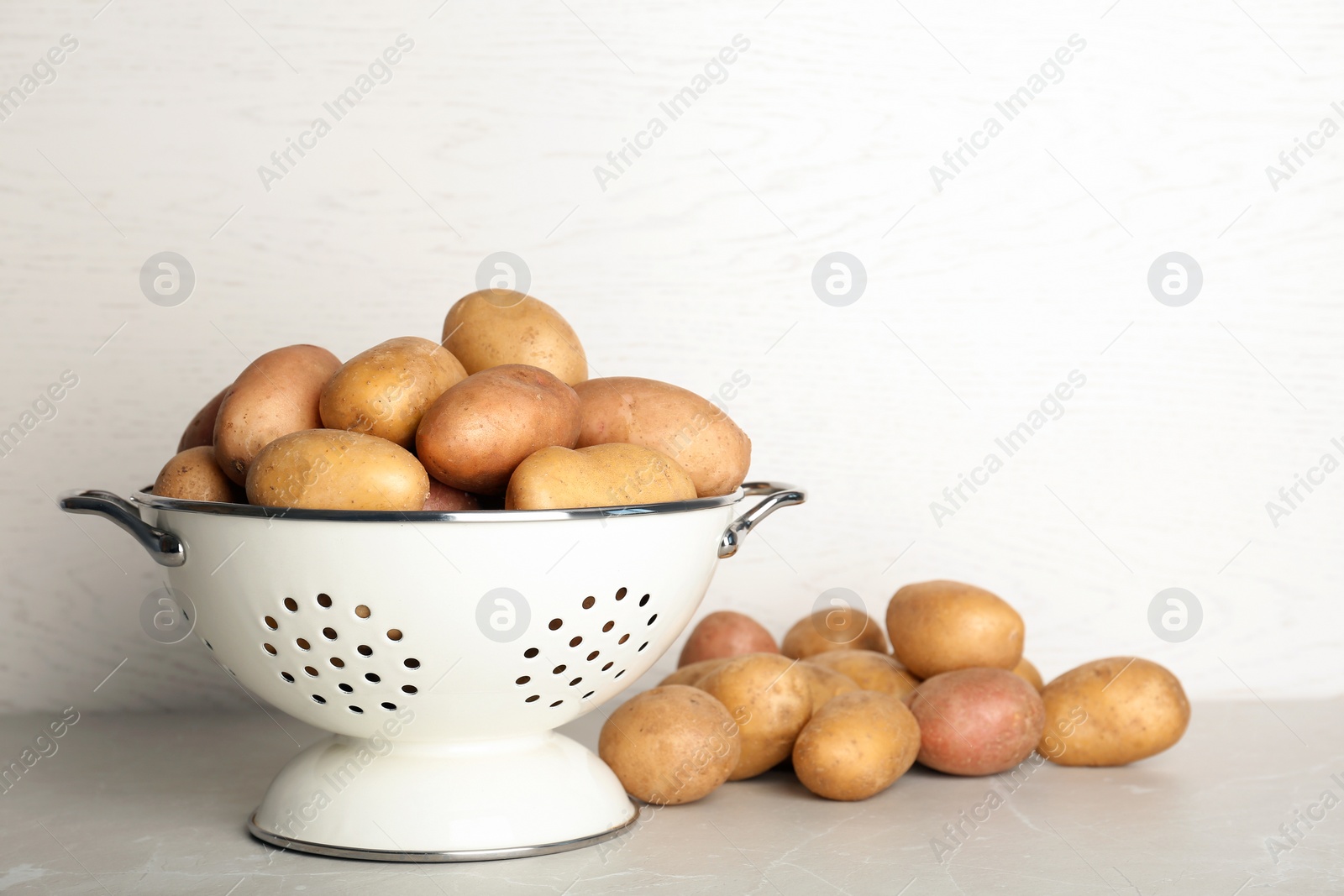 Photo of Colander with fresh ripe organic potatoes on table