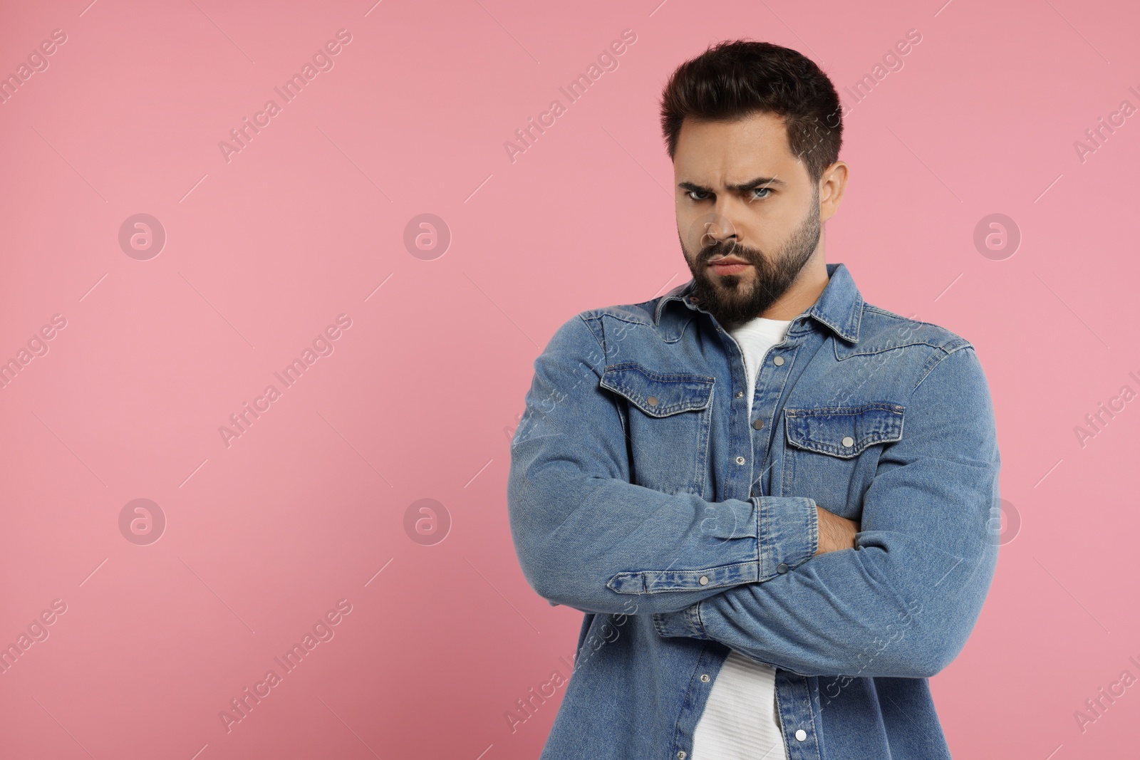 Photo of Portrait of resentful man with crossed arms on pink background, space for text