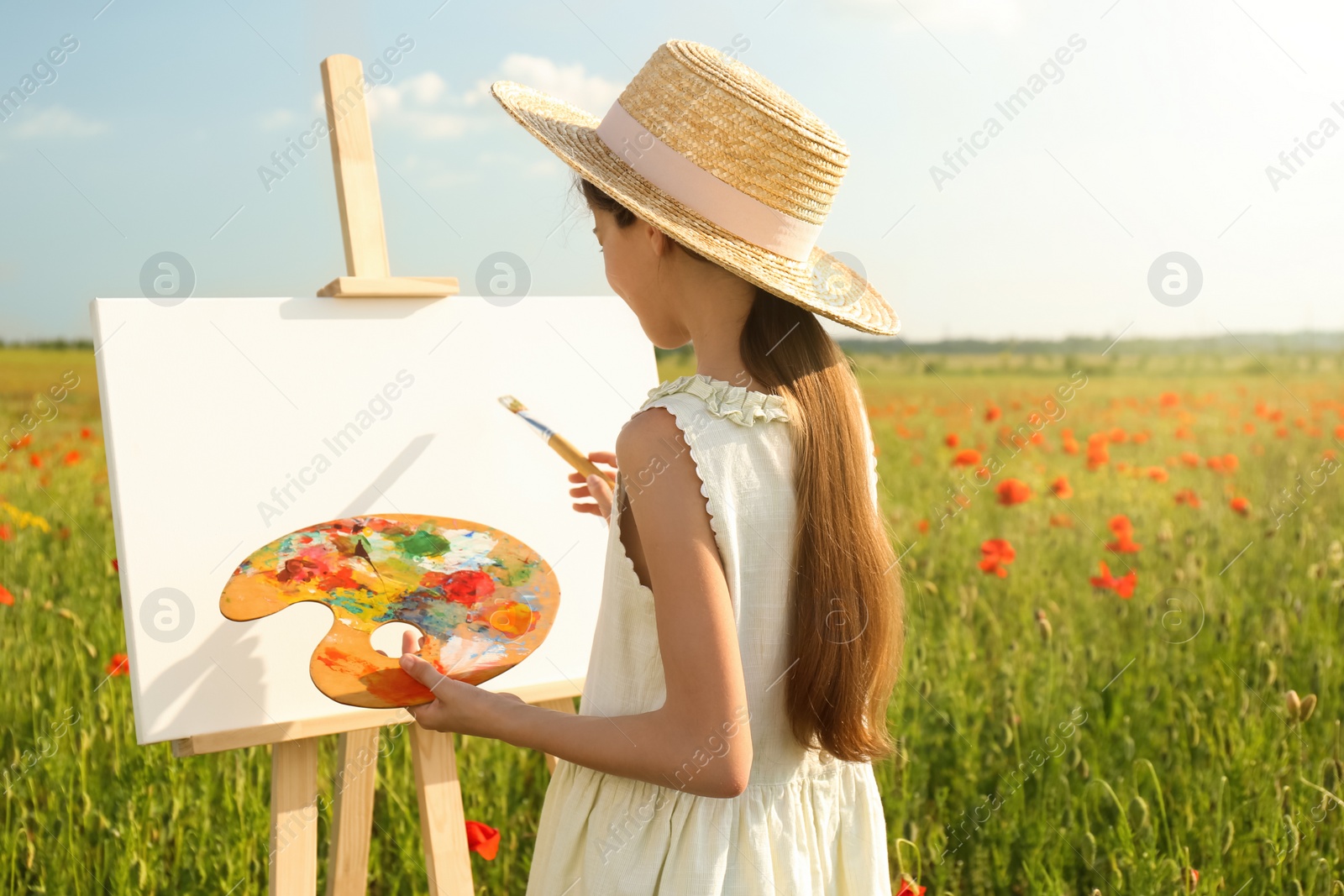 Photo of Little girl painting on easel in beautiful poppy field