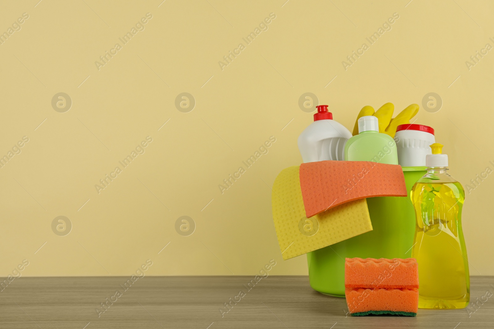 Photo of Bucket with different cleaning supplies on wooden floor near beige wall. Space for text