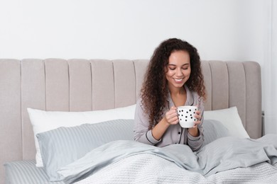 Beautiful African American woman with cup of drink in bed at home