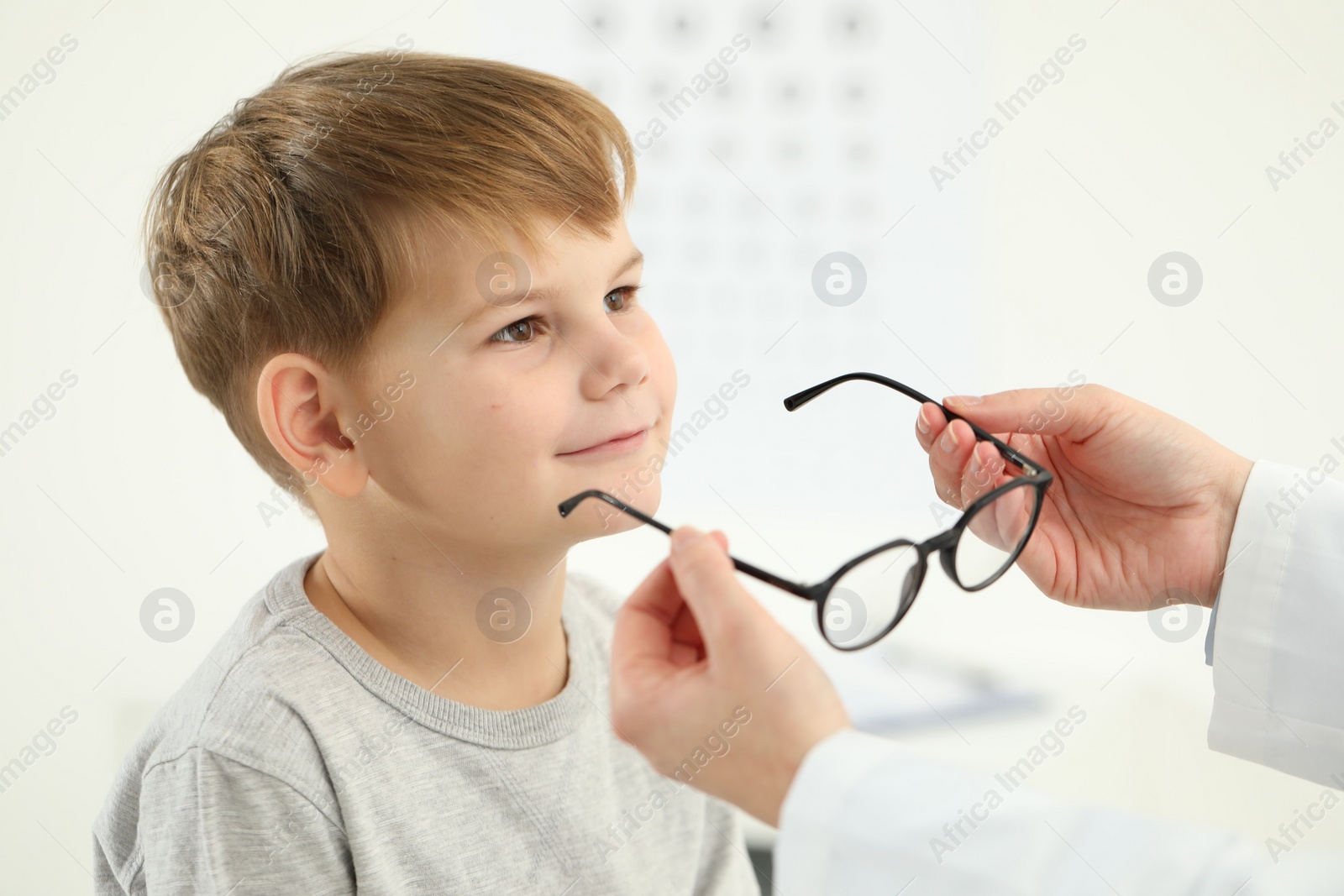 Photo of Vision testing. Ophthalmologist giving glasses to little boy indoors