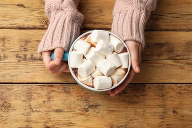 Photo of Woman with cup of tasty hot chocolate and marshmallows at wooden table, top view