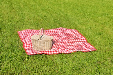 Photo of Picnic basket with checkered tablecloth on green grass outdoors