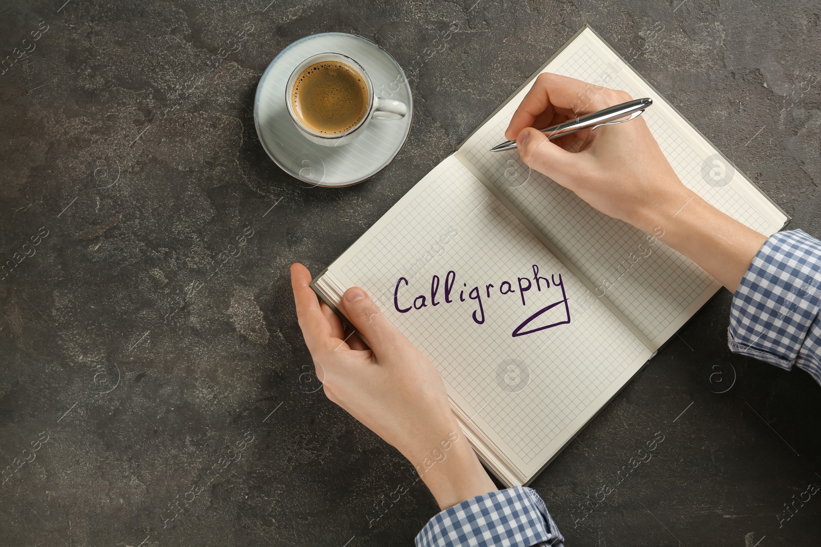 Image of Woman writing word Calligraphy in notebook at grey table, top view. Space for text