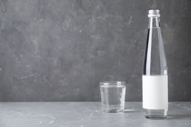 Photo of Bottle and glass with water on grey marble table, space for text