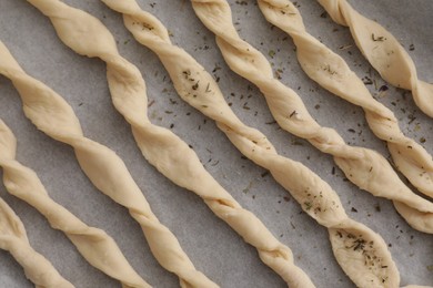 Photo of Homemade breadsticks with spices on baking sheet, flat lay. Cooking traditional grissini