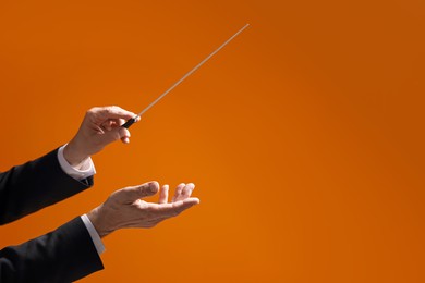 Professional conductor with baton on orange background, closeup. Space for text