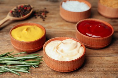 Photo of Ketchup, mustard, mayonnaise and ingredients on wooden table