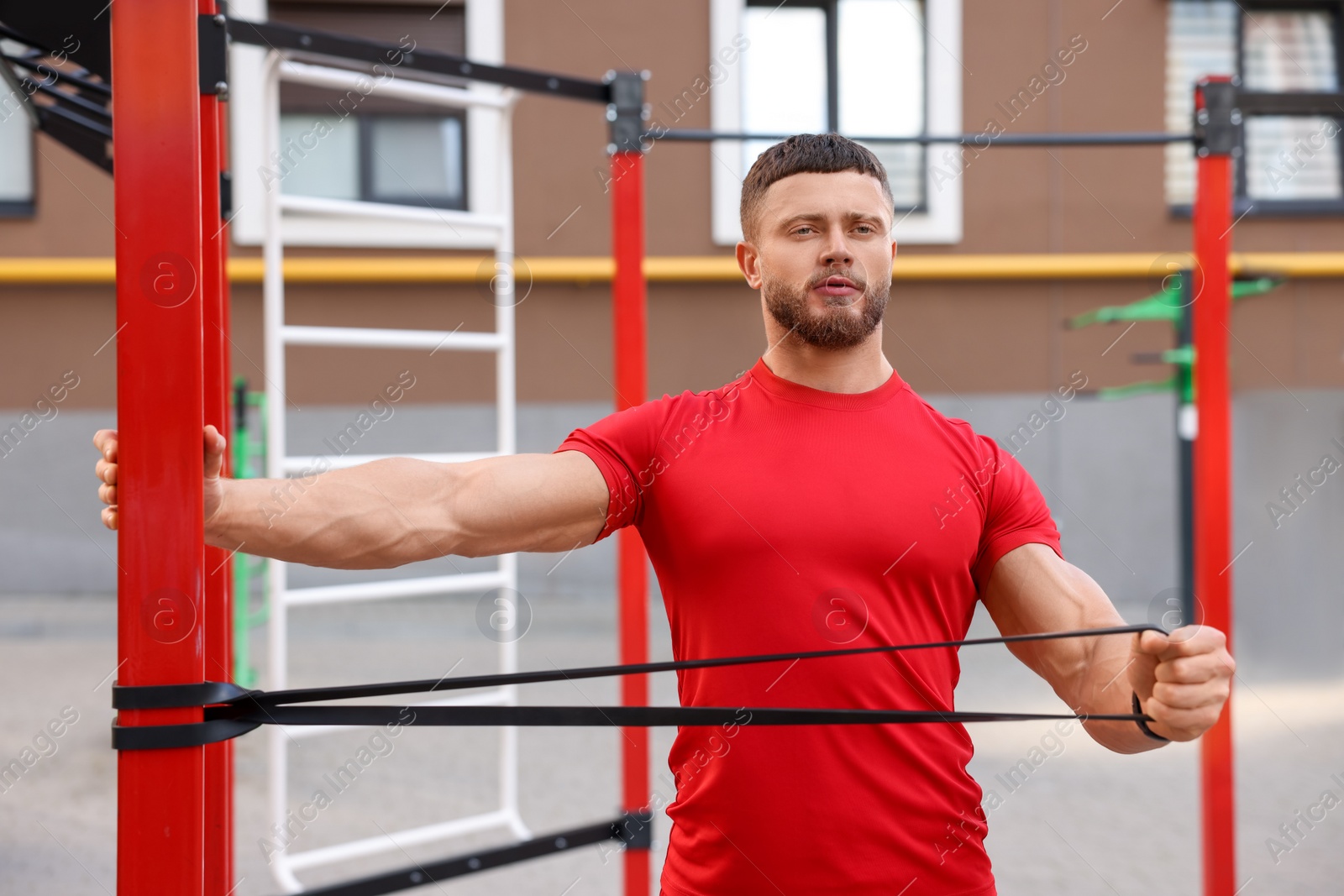 Photo of Muscular man doing exercise with elastic resistance band on sports ground