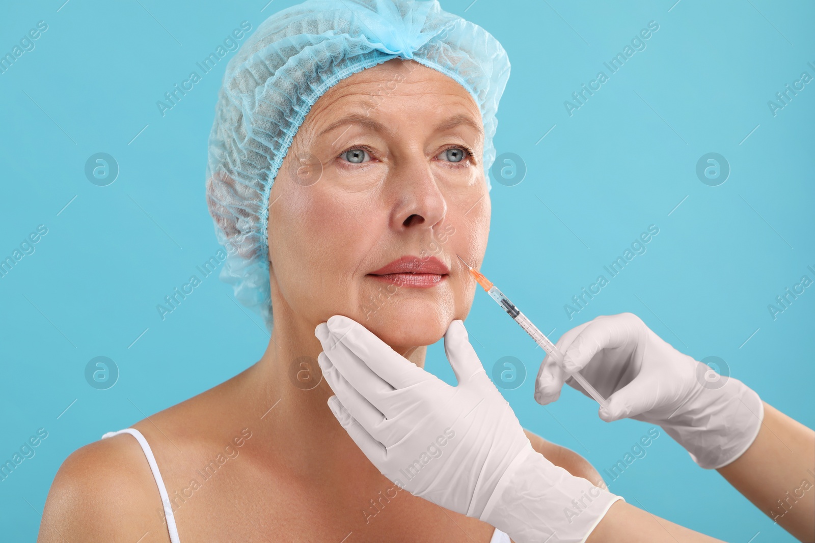 Photo of Doctor giving facial injection to senior woman on light blue background. Cosmetic surgery