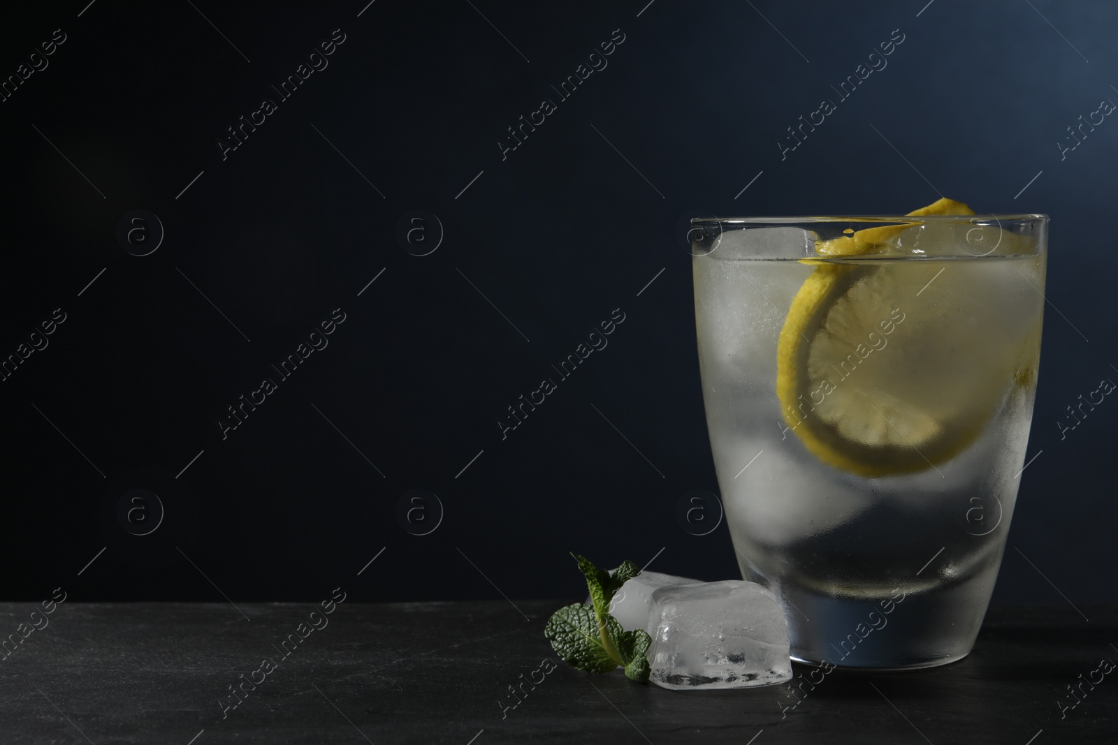 Photo of Shot of vodka with lemon, ice and mint on black table. Space for text