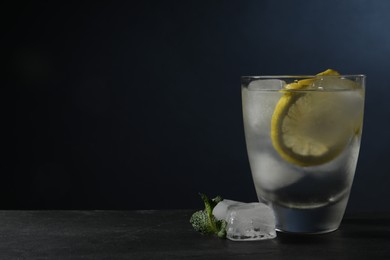 Photo of Shot of vodka with lemon, ice and mint on black table. Space for text