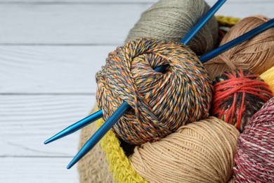 Photo of Soft woolen yarns and knitting needles on white wooden table, closeup. Space for text