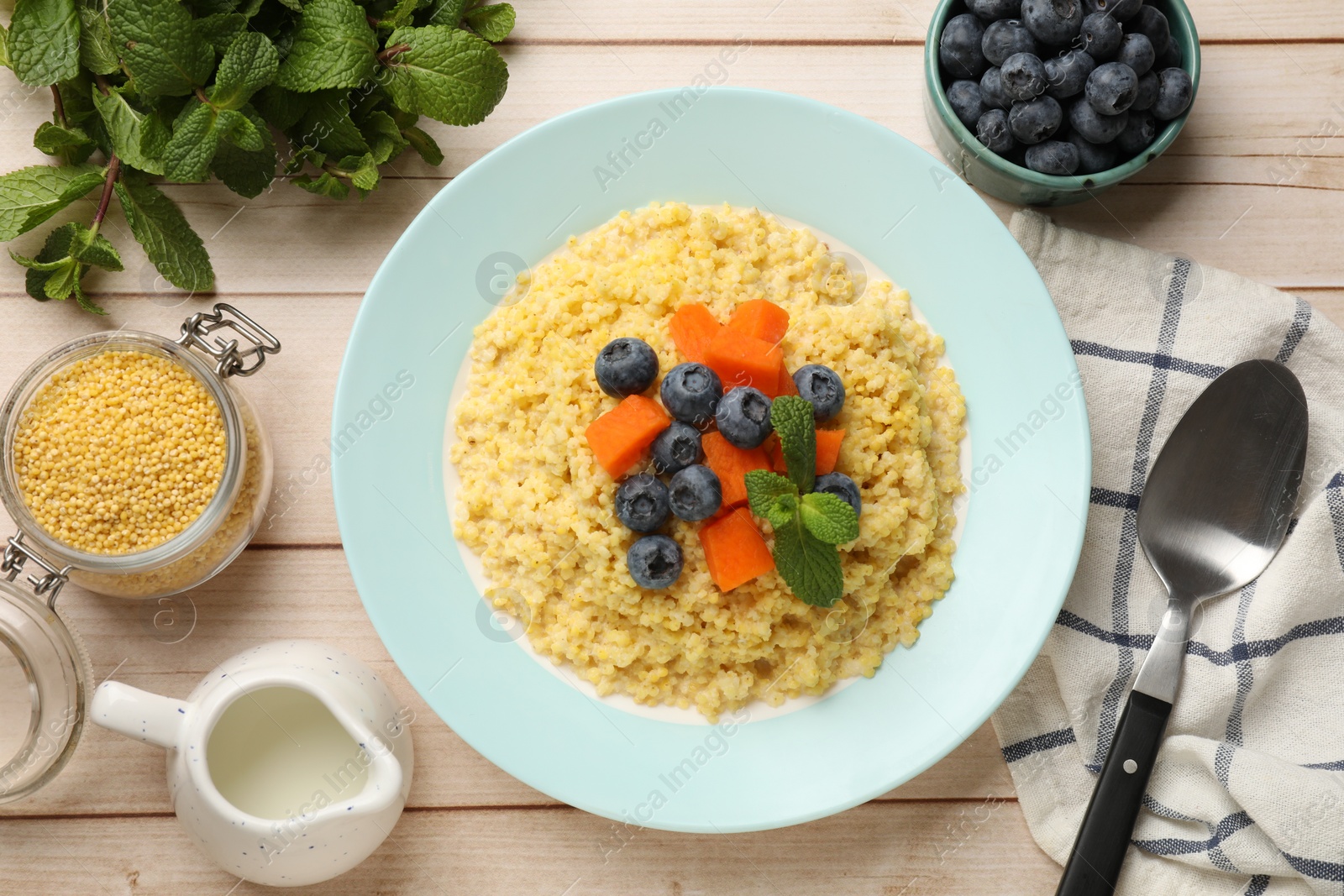 Photo of Plate with tasty millet porridge, blueberries, pumpkin and mint on light wooden table, flat lay