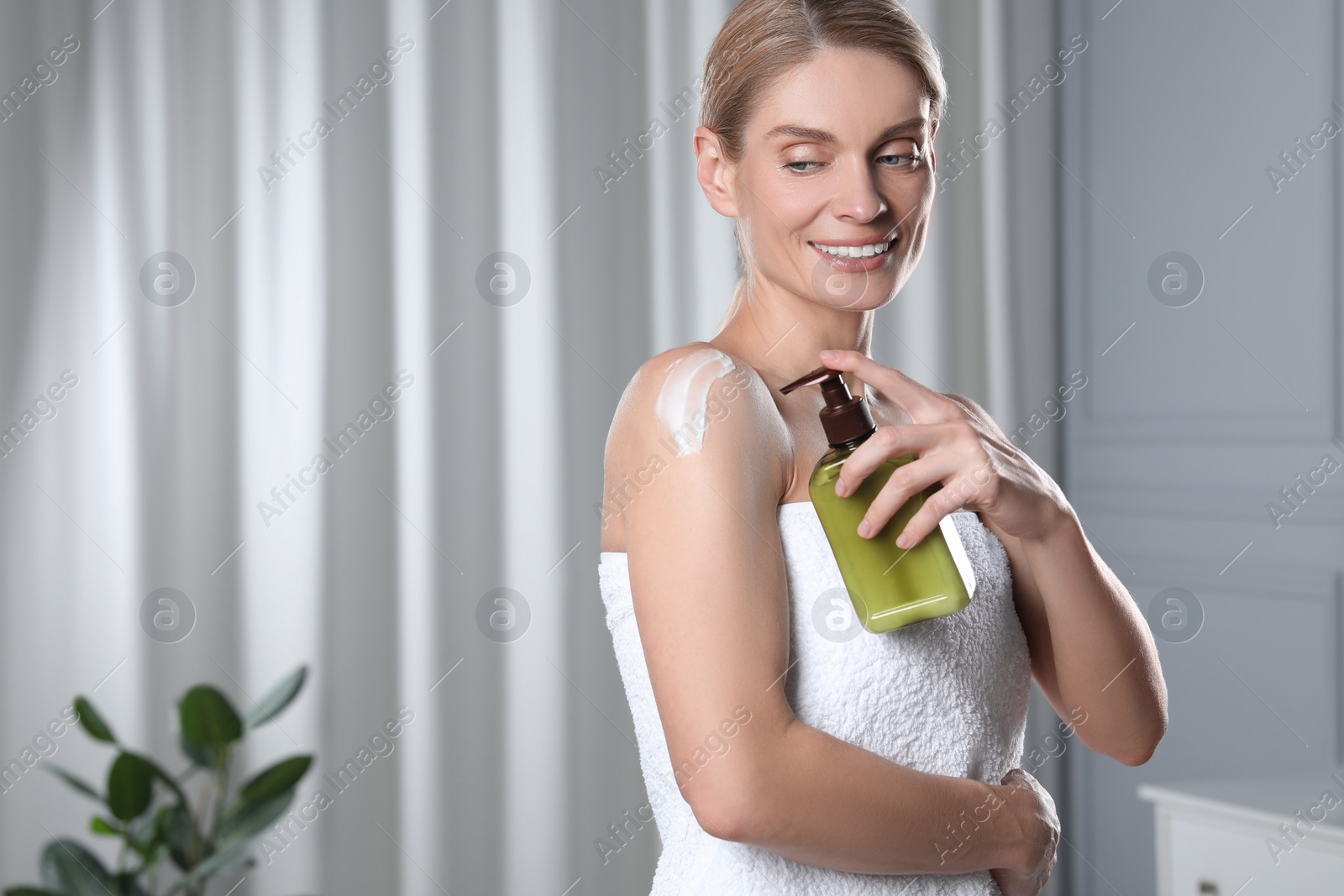 Photo of Happy woman applying body cream onto shoulder indoors, space for text