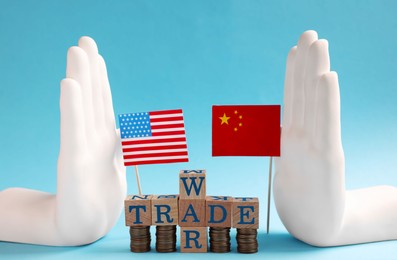 Photo of USA and China flags, coins and phrase Trade war made of wooden cubes on light blue background
