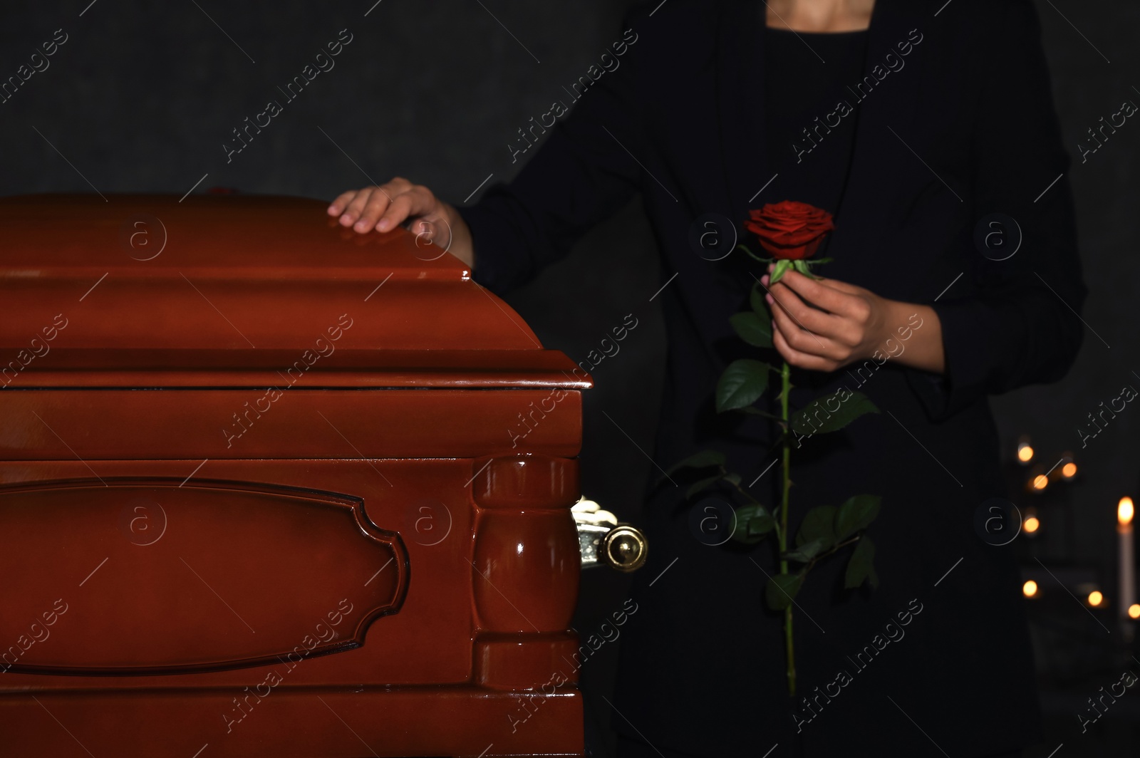 Photo of Young woman with red rose near casket in funeral home, closeup
