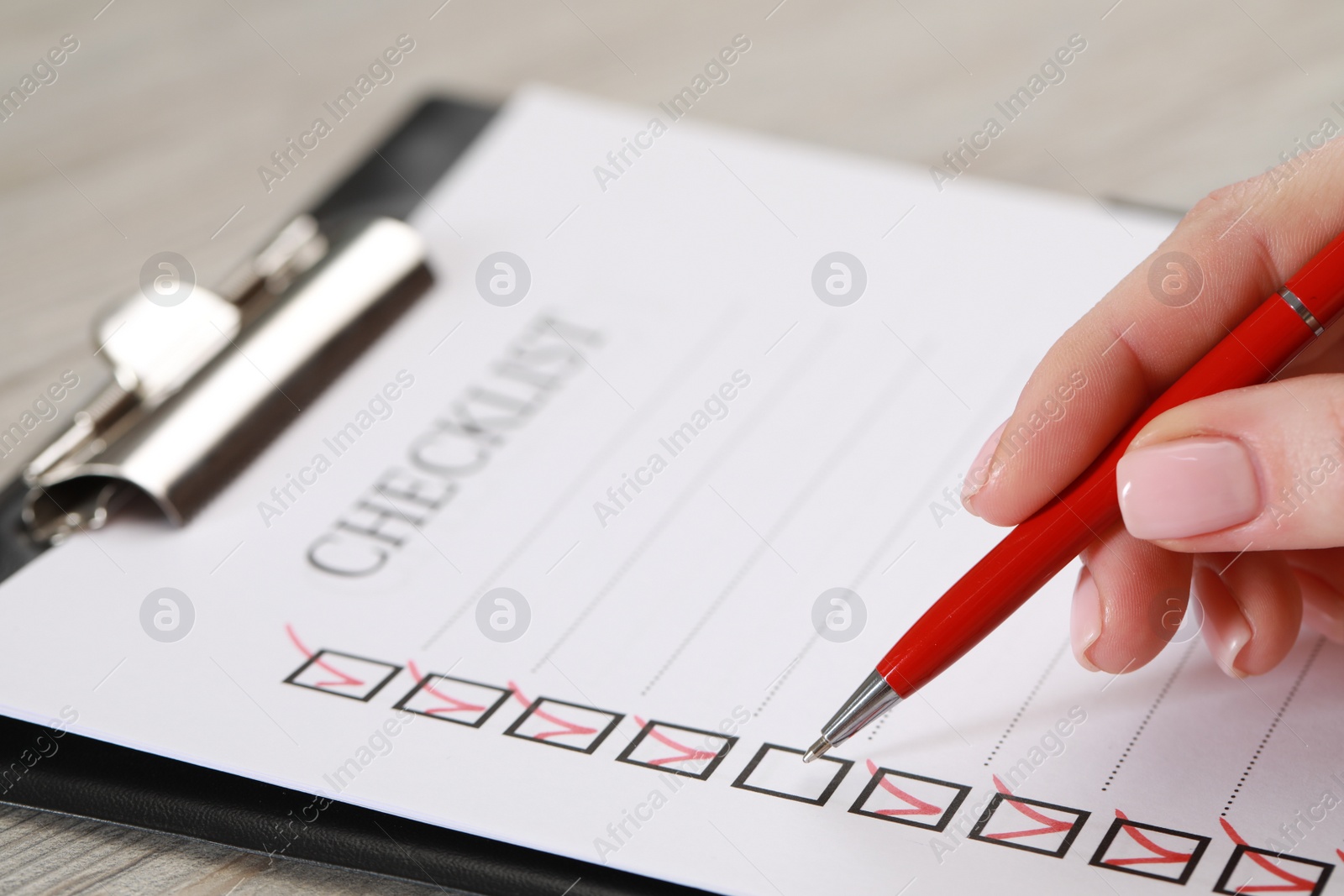 Photo of Woman filling Checklist at wooden table, closeup