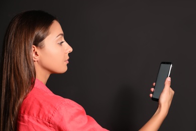 Young woman unlocking smartphone with facial scanner on black background. Biometric verification