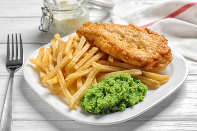 Plate with British traditional fish and potato chips on wooden background