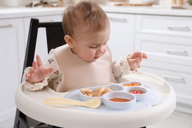 Photo of Cute little baby eating food in high chair at kitchen