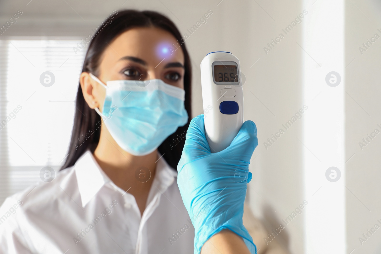 Image of Doctor measuring woman's temperature in office, closeup. Prevent spreading of Covid-19