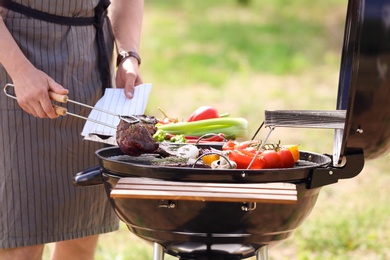 Photo of Young man cooking meat and vegetables on barbecue grill outdoors