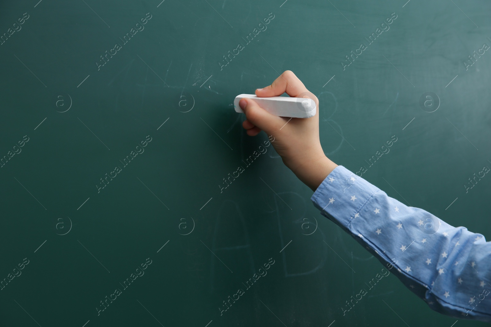 Photo of Little child writing on chalkboard, closeup. Space for text