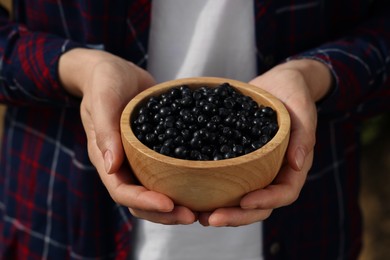 Photo of Woman holding wooden bowl of bilberries, closeup