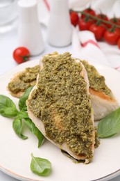 Delicious chicken breasts with pesto sauce and basil on table, closeup
