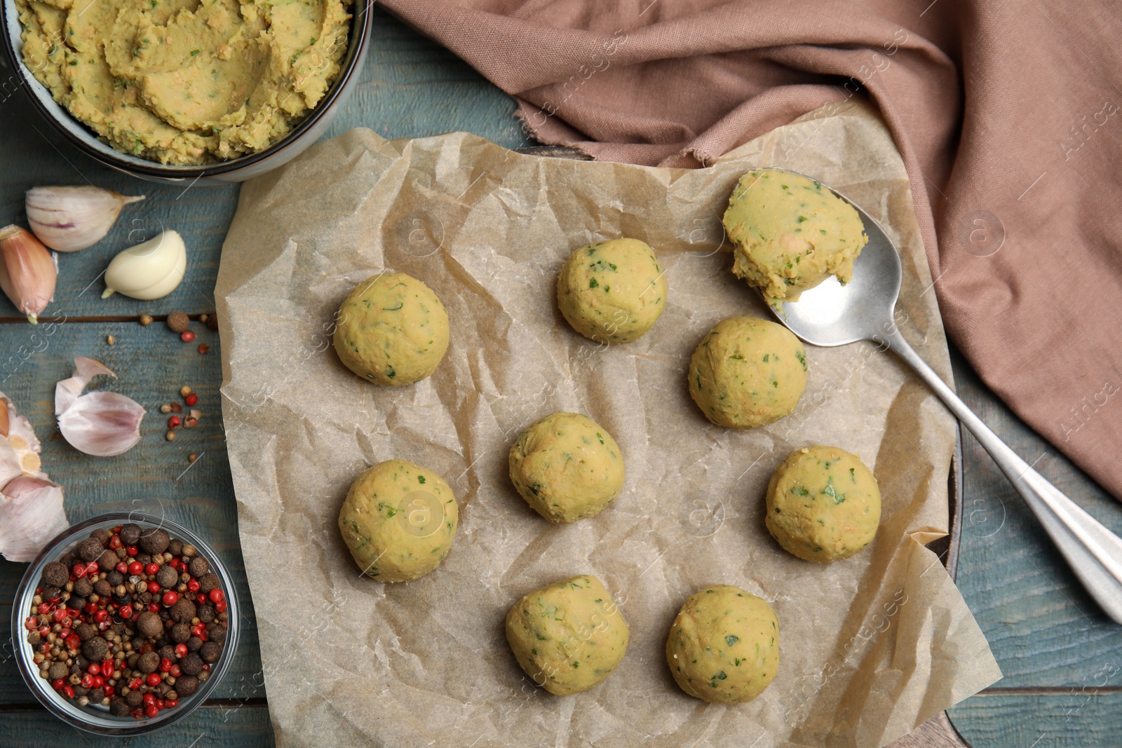 Photo of Raw falafel balls and ingredients on light blue wooden table, flat lay