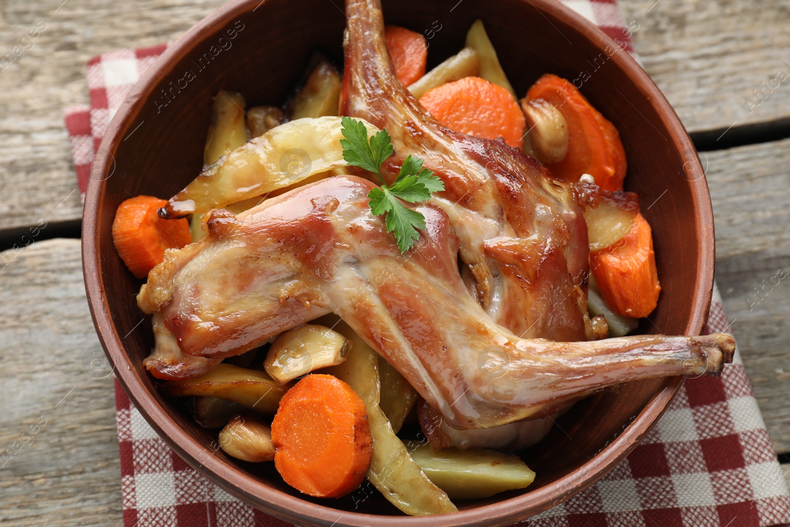 Photo of Tasty cooked rabbit with vegetables in bowl on wooden table, closeup