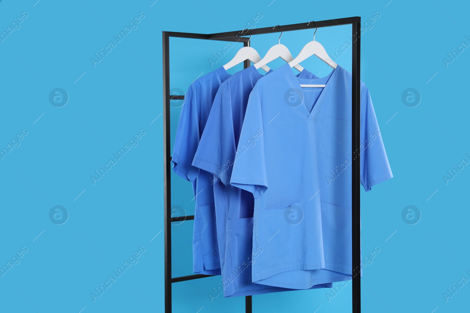 Photo of Medical uniforms on metal rack against light blue background. Space for text